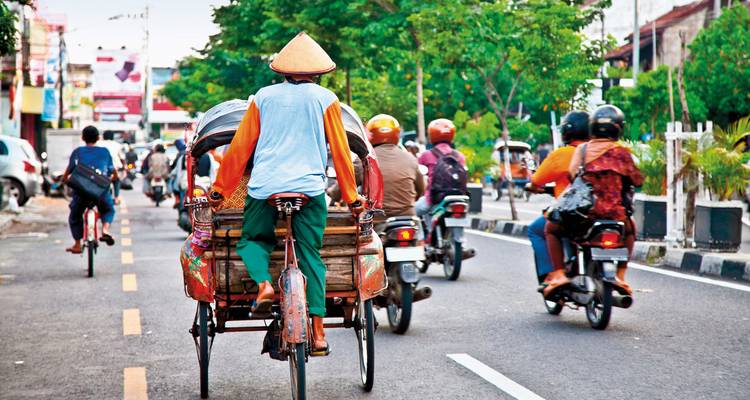 A street scene in Indonesia with people riding bicycles and motorcycles.