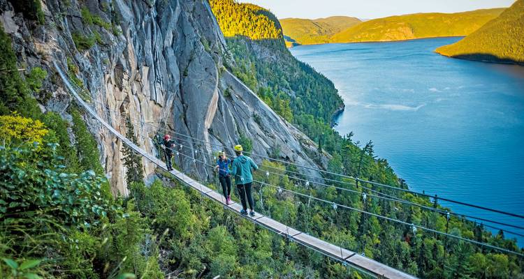 Des gens sur un pont suspendu avec vue sur une falaise et une rivière.