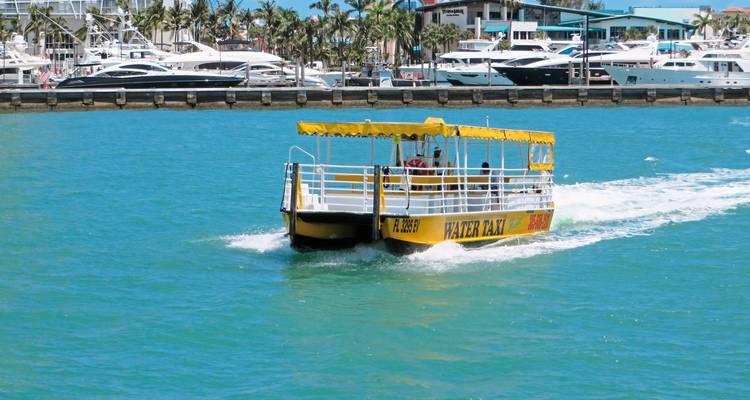 Barco turístico navegando por una vía fluvial con yates al fondo.