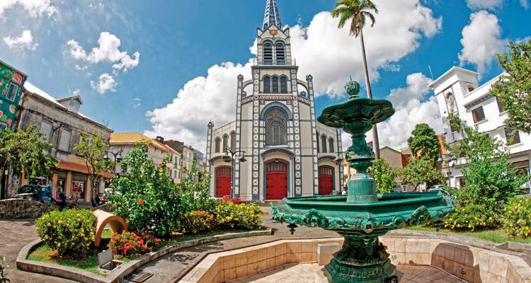 Kirche mit einem Brunnen im Vordergrund und Palmen.