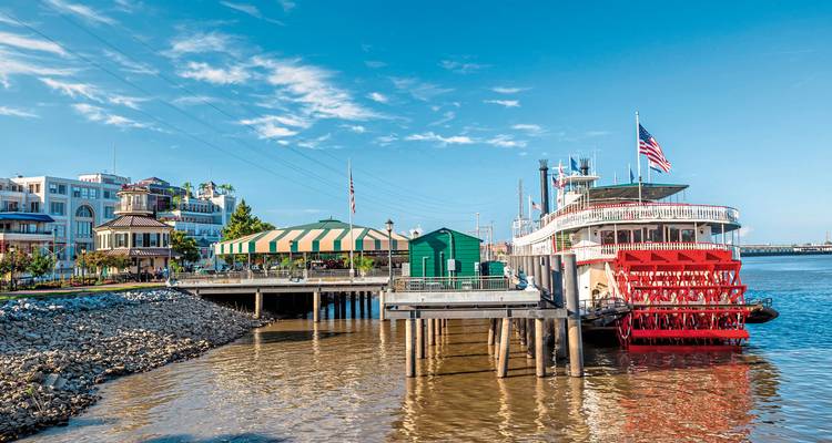 A riverboat docked at a wooden pier by a restaurant.