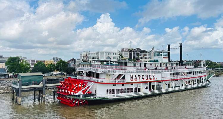 Historische stoomboot Natchez aangelegd aan de Mississippi-rivier met stadsgebouwen en bewolkte hemel op de achtergrond.
