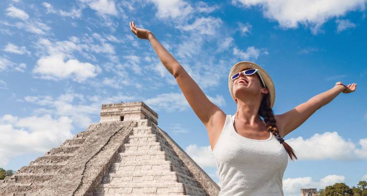 A woman celebrating with raised arms in front of a Mayan pyramid.