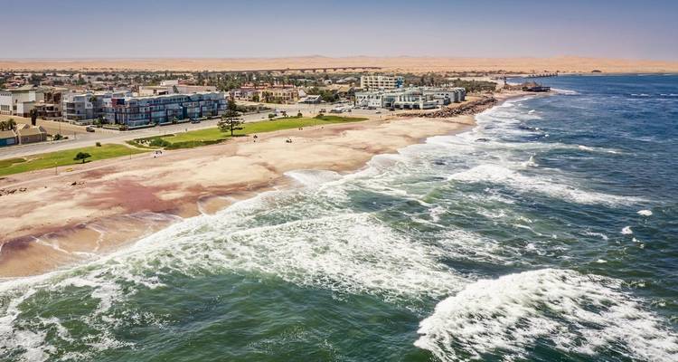 Luchtfoto van Swakopmund's zandige kustlijn waar Atlantische golven de gebouwen van de woestijnstad ontmoeten.