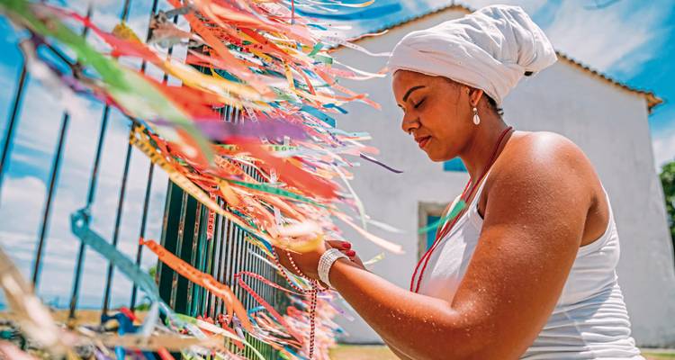 A person tying colorful ribbons to a fence in a sunny setting.