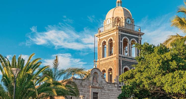 A stone church tower set against a bright blue sky with palm trees.