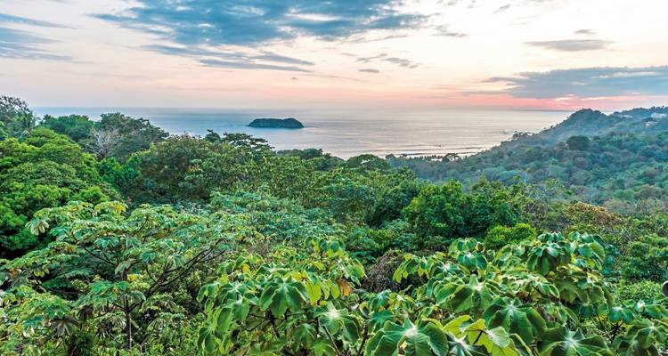 Sunset view over lush green hills and an ocean.