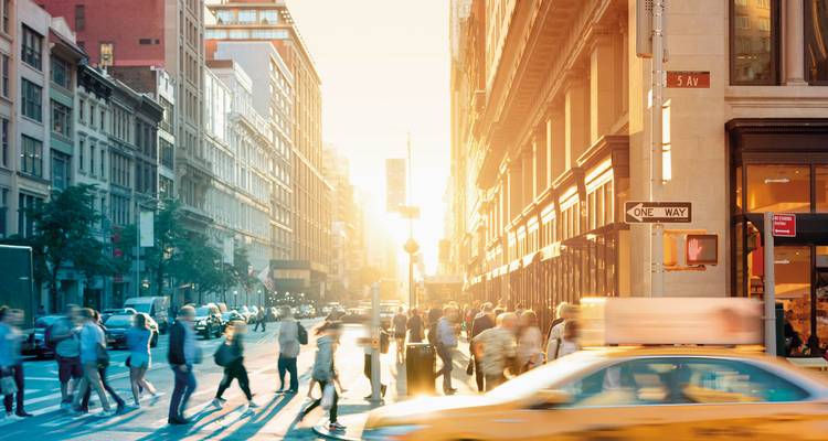 Rue animée de la ville avec un taxi et des piétons au coucher du soleil.