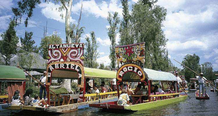 Des bateaux colorés avec des passagers sur un canal bordé d'arbres.