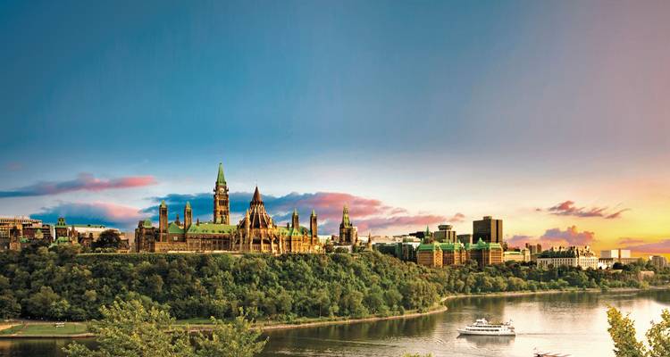 Parliament buildings on a hill overlooking a river at sunset.