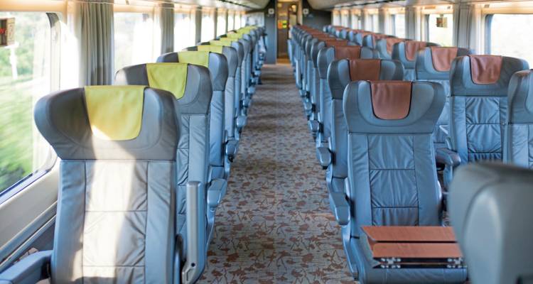 Intérieur de train vide avec des sièges bleus et la lumière du soleil qui entre.