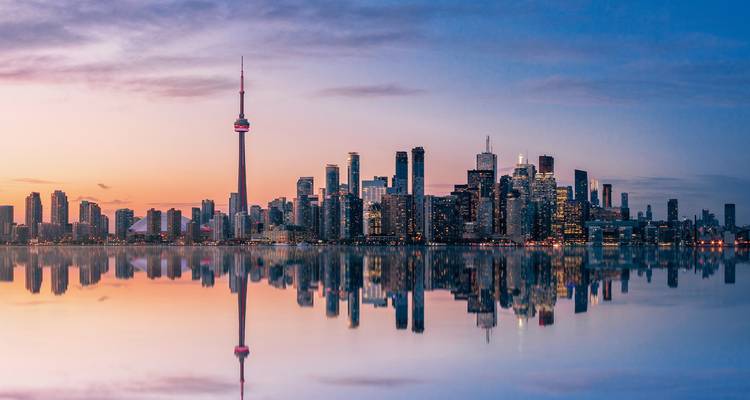 Horizon urbain au coucher du soleil reflété dans l'eau avec une tour proéminente.
