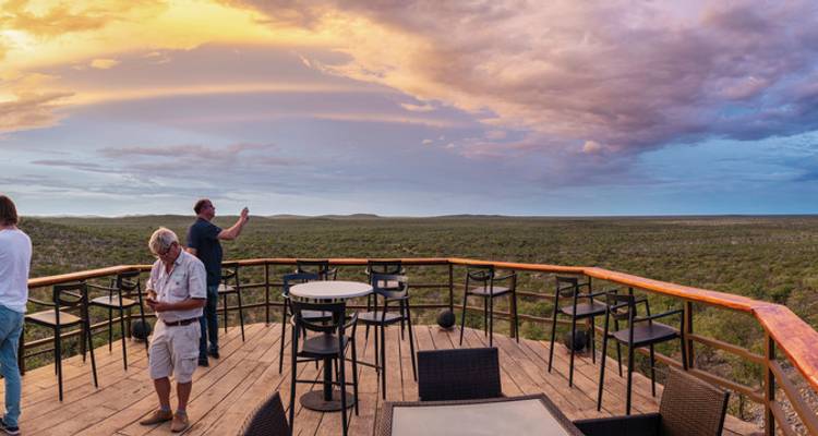 People enjoying the view from a wooden deck at sunset.