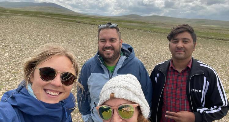Four travelers smiling for a selfie on a wide stony plateau under cloudy skies.