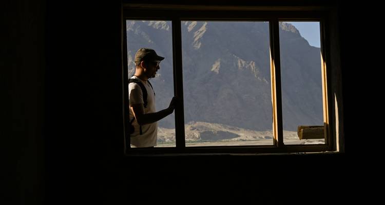 Silhouette of a man framed by a window looking out to rugged mountains.