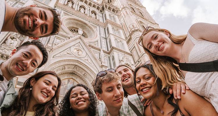 Lächelnde Freunde drängen sich für ein Selfie unter der kunstvollen Marmorfassade des Doms von Florenz zusammen.
