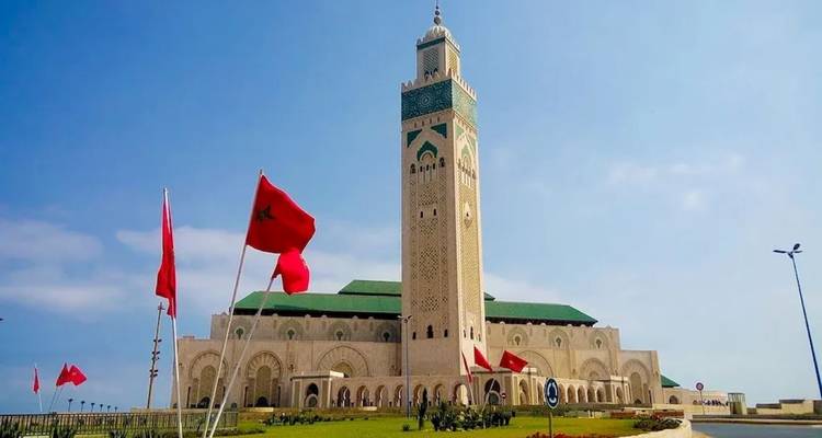 Die Hassan-II-Moschee in Casablanca mit marokkanischen Flaggen und klarem blauen Himmel.