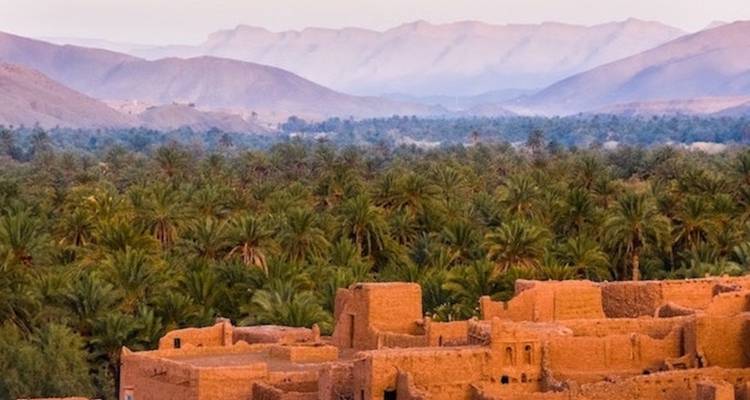 Alte Kasbah-Strukturen mit Palmen und Bergen in der Abenddämmerung.