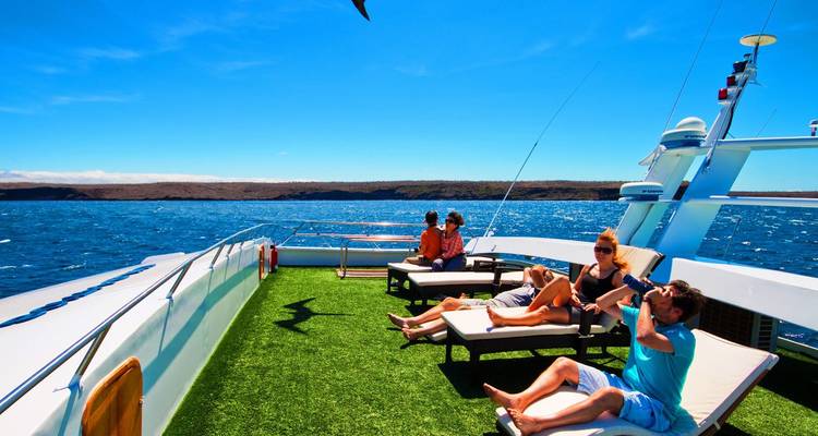 Travellers relaxing on sun-loungers aboard a modern yacht deck cruising on deep blue ocean waters under a bright sky
