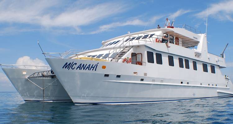 White twin-hulled catamaran named “M/C Anahí” floating on calm blue sea with light clouds overhead
