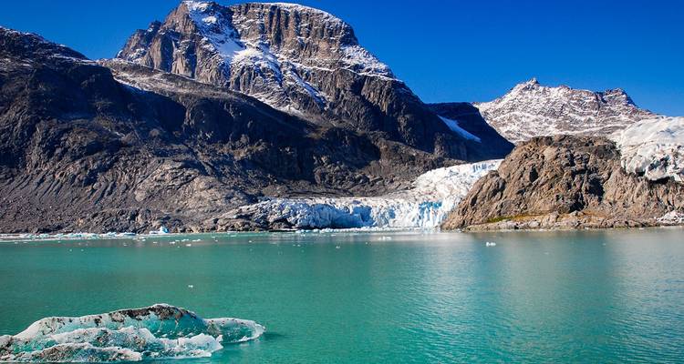 A bright glacier spills into vivid turquoise waters beneath rugged granite mountains.