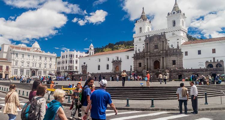 Bustling Plaza de San Francisco in Quito with colonial church façades and crowds under bright blue skies.