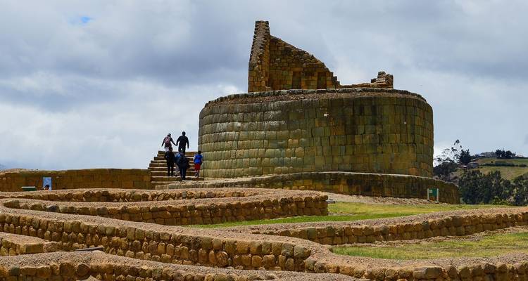 Visitors explore circular stone temple ruins of Ingapirca beneath overcast Andean skies.