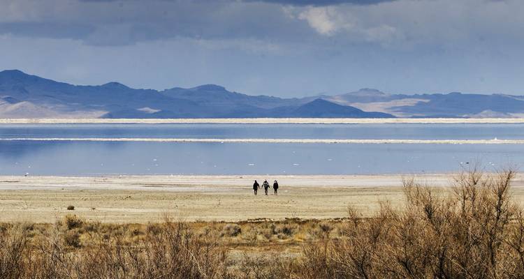 Vaste paysage de lac salé avec trois marcheurs au loin sous un ciel nuageux dramatique