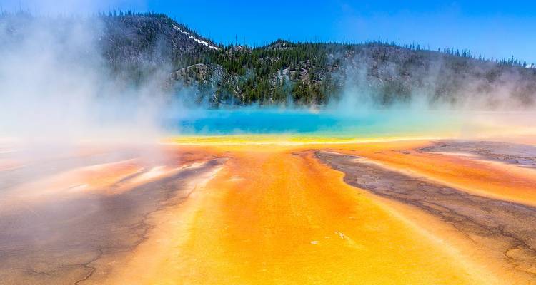 Colores del arcoíris vibrantes de una fuente termal humeante rodeada de colinas boscosas