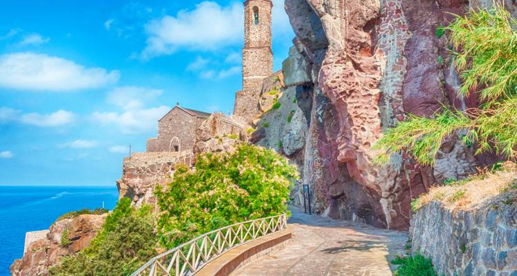 Sentier côtier accidenté menant à une ancienne église perchée sur une falaise.