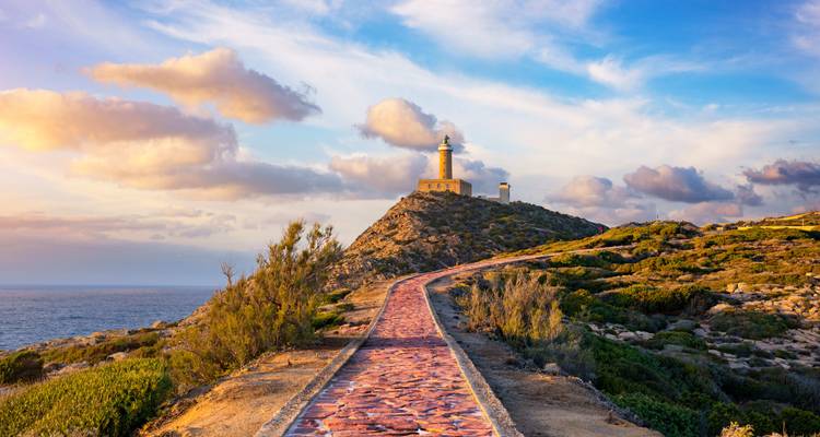 Phare sur une colline avec vues panoramiques sur l'océan au coucher du soleil.