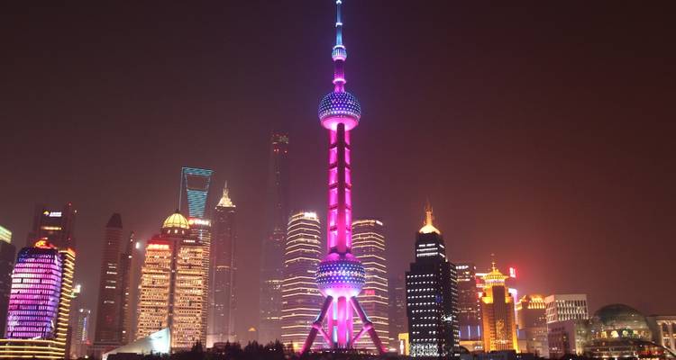 Modern skyscraper skyline with a prominent tower lit up at night.