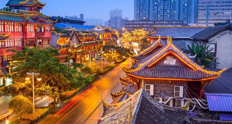Traditional Chinese street with brightly lit shops and trees.