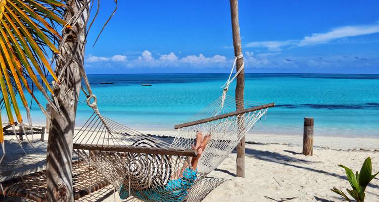 Personne se relaxant dans un hamac sur une plage tropicale avec une eau bleue claire.