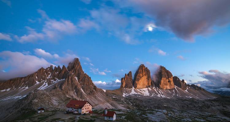 Dramatische toppen van Tre Cime di Lavaredo die bij schemering boven een bergrefugium gloeien.