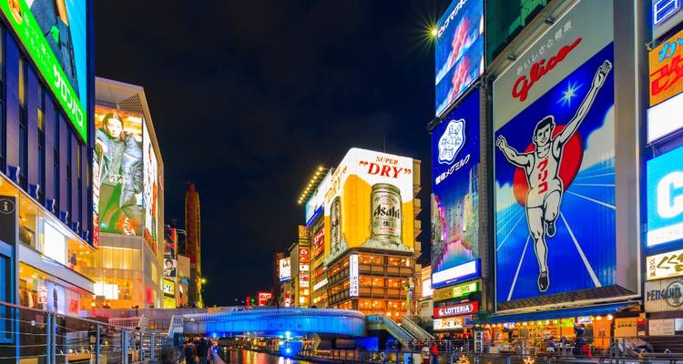 Le quartier de Dotonbori illuminé par des enseignes au néon avec des panneaux publicitaires colorés se reflétant sur le canal la nuit