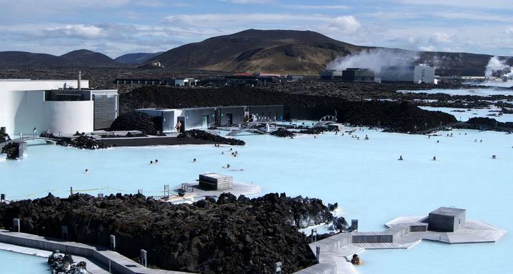 Uitgebreid uitzicht over de bleke geothermische wateren van Blue Lagoon met badgasten en een vulkanisch landschap op de achtergrond.