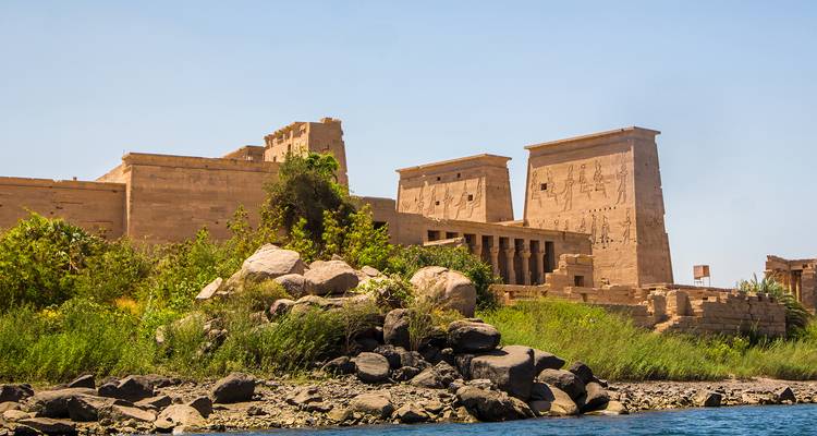 Oud zandstenen tempelcomplex op een eiland, omlijst door weelderige vegetatie en de Nijl.