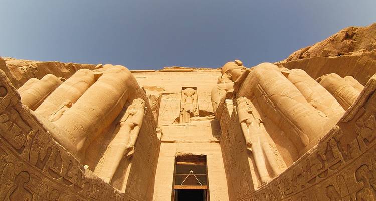 Massieve standbeelden van Farao Ramses flankeren de ingang van de Abu Simbel tempel onder een wolkenloze hemel.