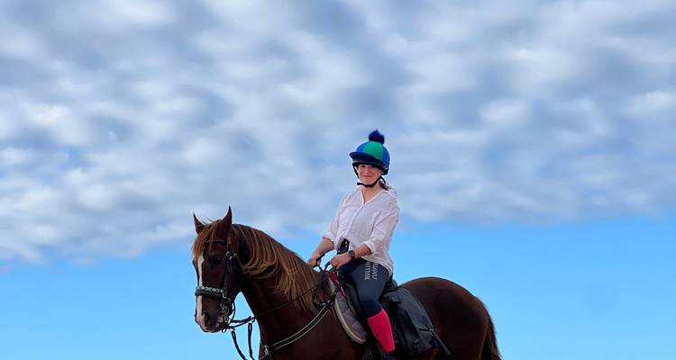 Person, die unter einem blauen bewölkten Himmel auf einem Pferd reitet.