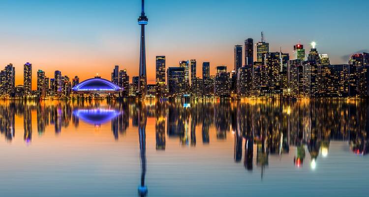 Horizon de Toronto au coucher de soleil avec la Tour CN et le Rogers Centre reflétés dans les eaux calmes du lac.