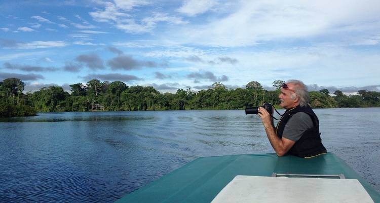Mann mit einer Kamera auf einem Boot, der über einen breiten Fluss blickt.