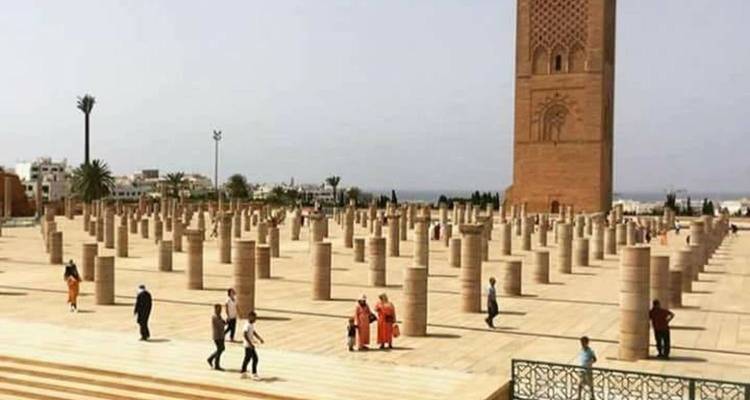 Open plaza of stone columns surrounding the Hassan Tower with scattered visitors on a hazy day