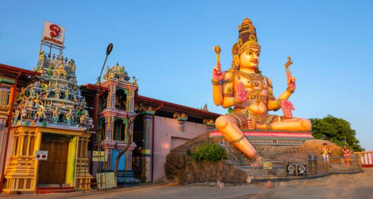 Eine hell bemalte Hindu-Götterstatue, die einen Tempelinnenhof unter klarem blauen Himmel in Sri Lanka beherrscht.
