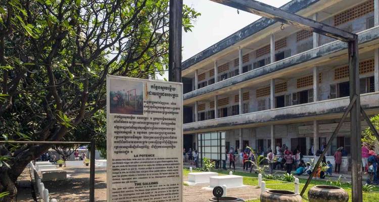Außenansicht des Tuol-Sleng-Genozid-Museums mit Informationstafel und Besuchern im Hof.
