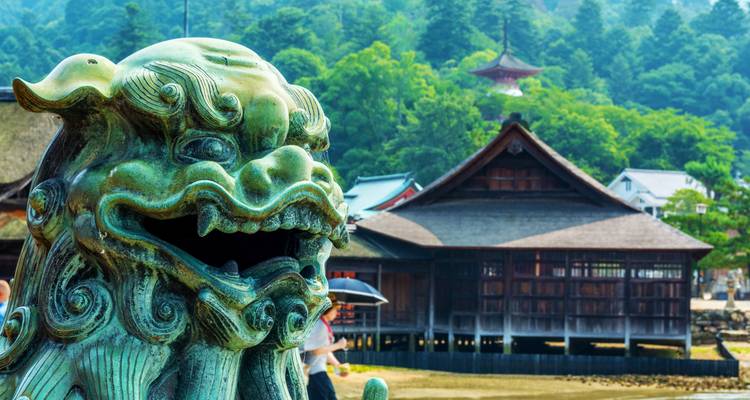 Bronze guardian lion statue overlooking traditional wooden shrine buildings on a green island