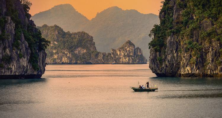 Bateau naviguant dans la baie d'Halong au coucher du soleil.