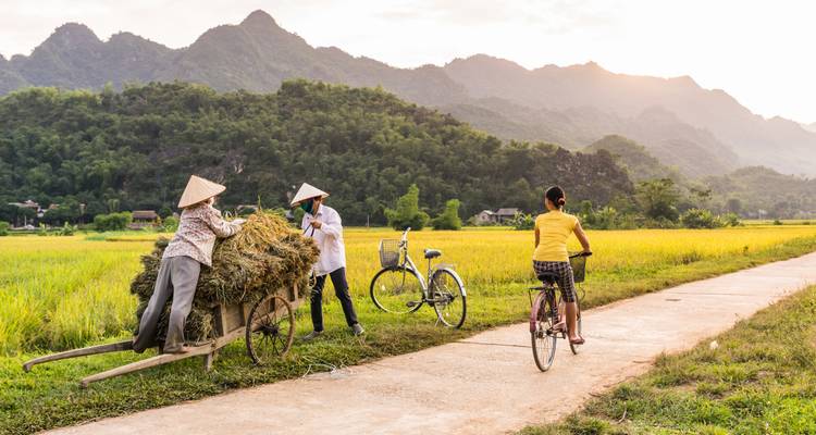 Des personnes à vélo interagissant avec les habitants locaux dans un cadre rural.