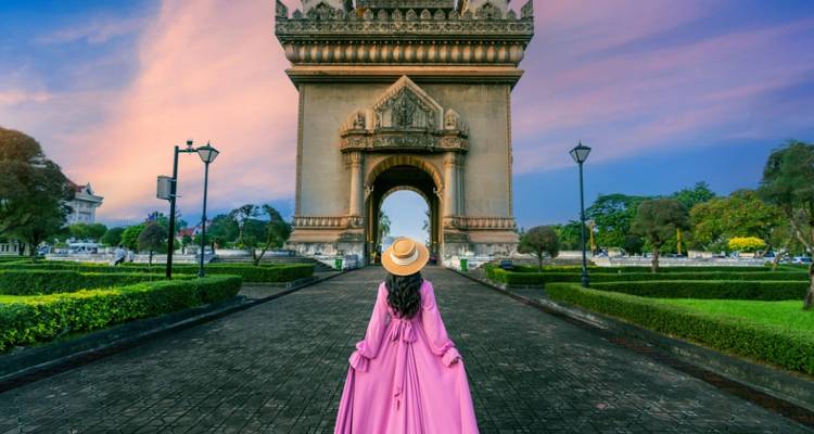 Voyageuse en robe rose fluide face au Monument de la Victoire Patuxai au coucher du soleil