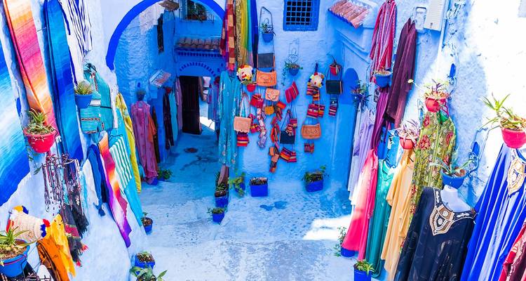 Vibrant blue alleyway lined with colorful textiles, bags and pottery in a Moroccan mountain town.